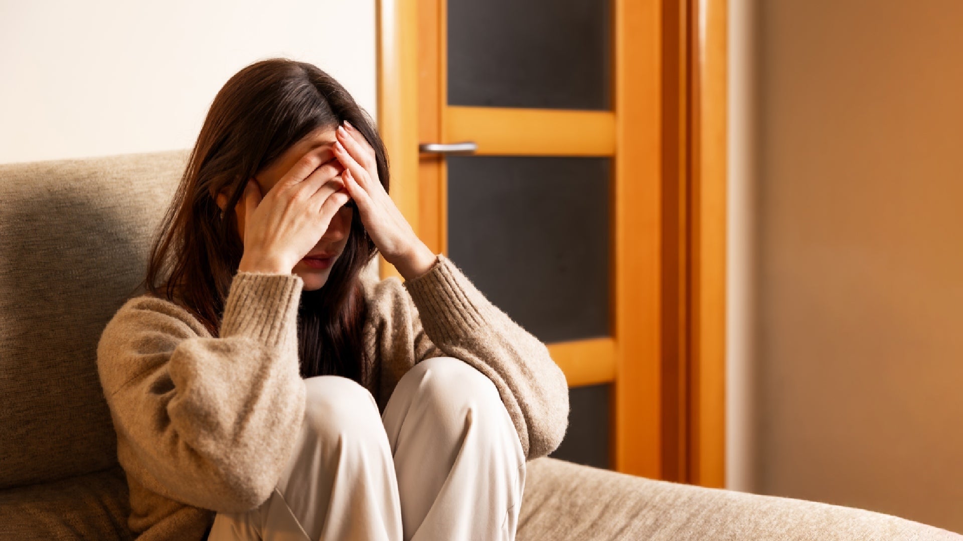 En kvinne med mørkt hår sitter i en sofa og tar hendene til ansiktet